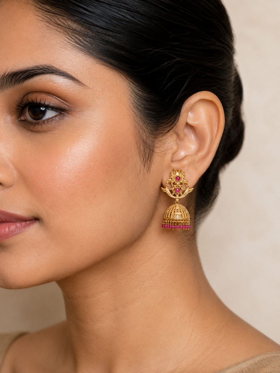 Model wearing an antique gold floral jhumka earring with ruby accents, profile view