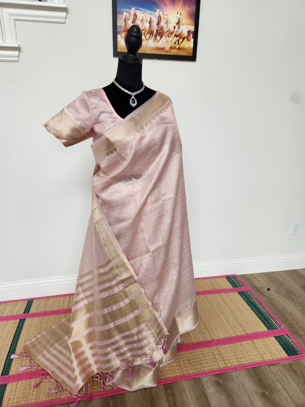 Natural-light photo of the baby pink tissue organza saree, front view, with gold zari border and striped tasseled pallu