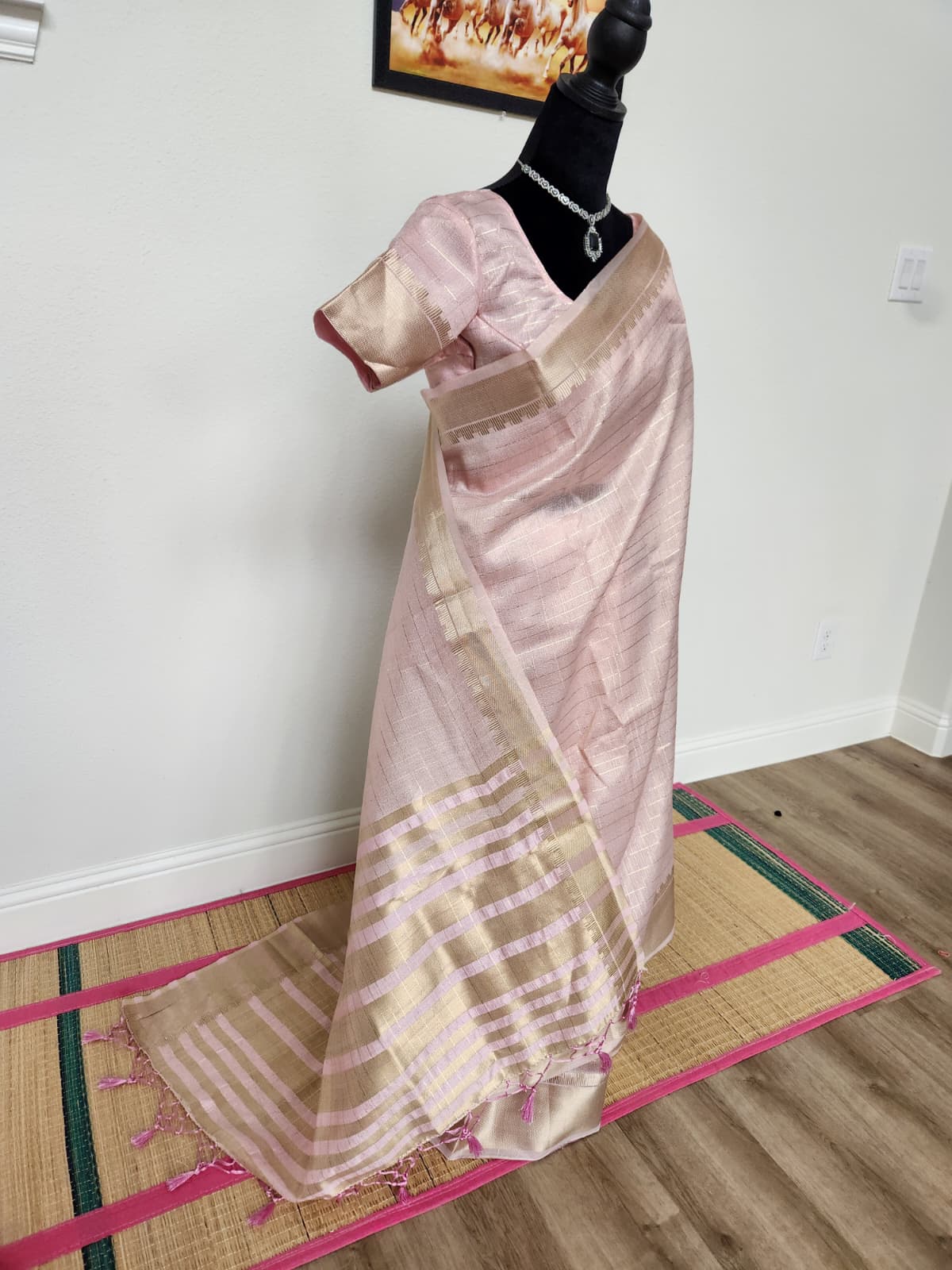 Natural-light side angle of the baby pink tissue organza saree showing the drape, gold zari border and tasseled pallu