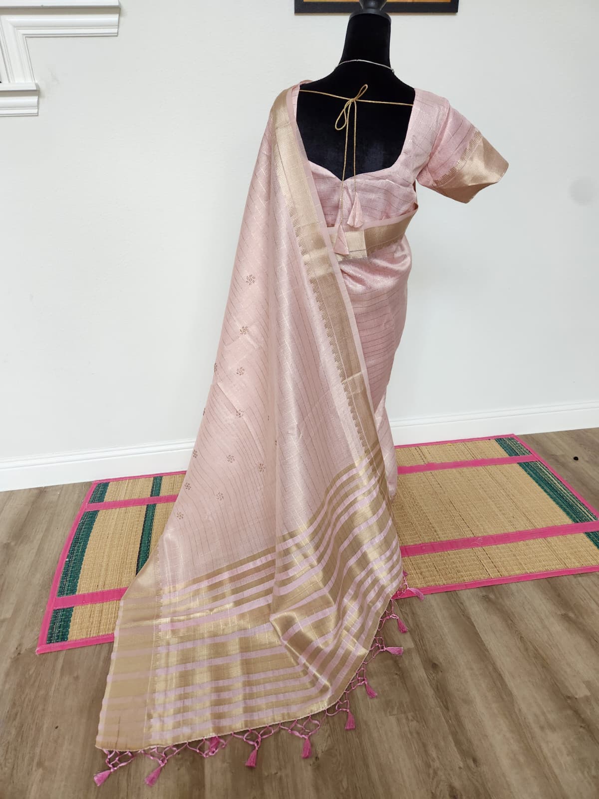 Natural-light full back view of the baby pink tissue organza saree with the pallu trailing and pink tassels at the edge